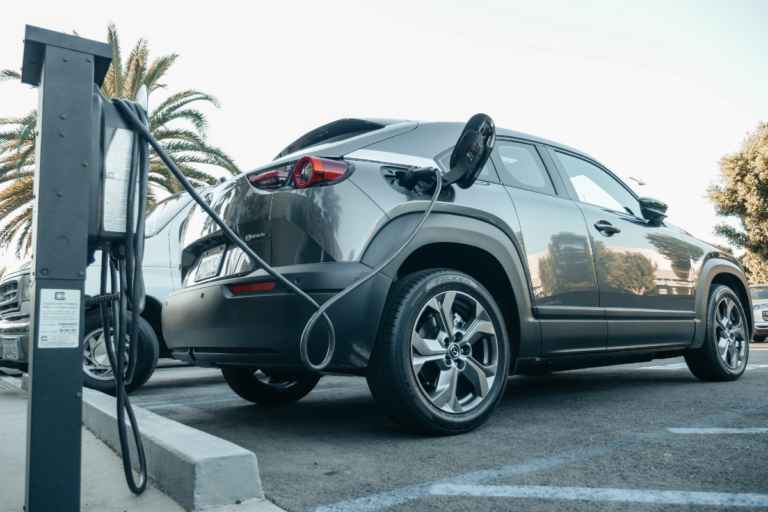 imagem de um carro elétrico preto parado em uma vaga e recarregando.
